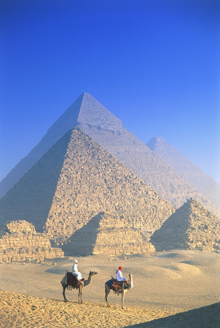 Two people on camels in front of Egyptian pyramids.