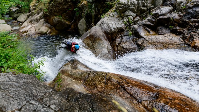 A high angle shot of people canyoning through a stream on the side of a mountain in France