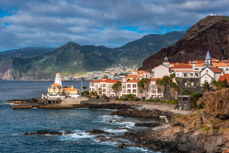 Marina da Quinta Grande, Madeira, Portugal. Seaside small village with lighthouse on rocky cliffs.